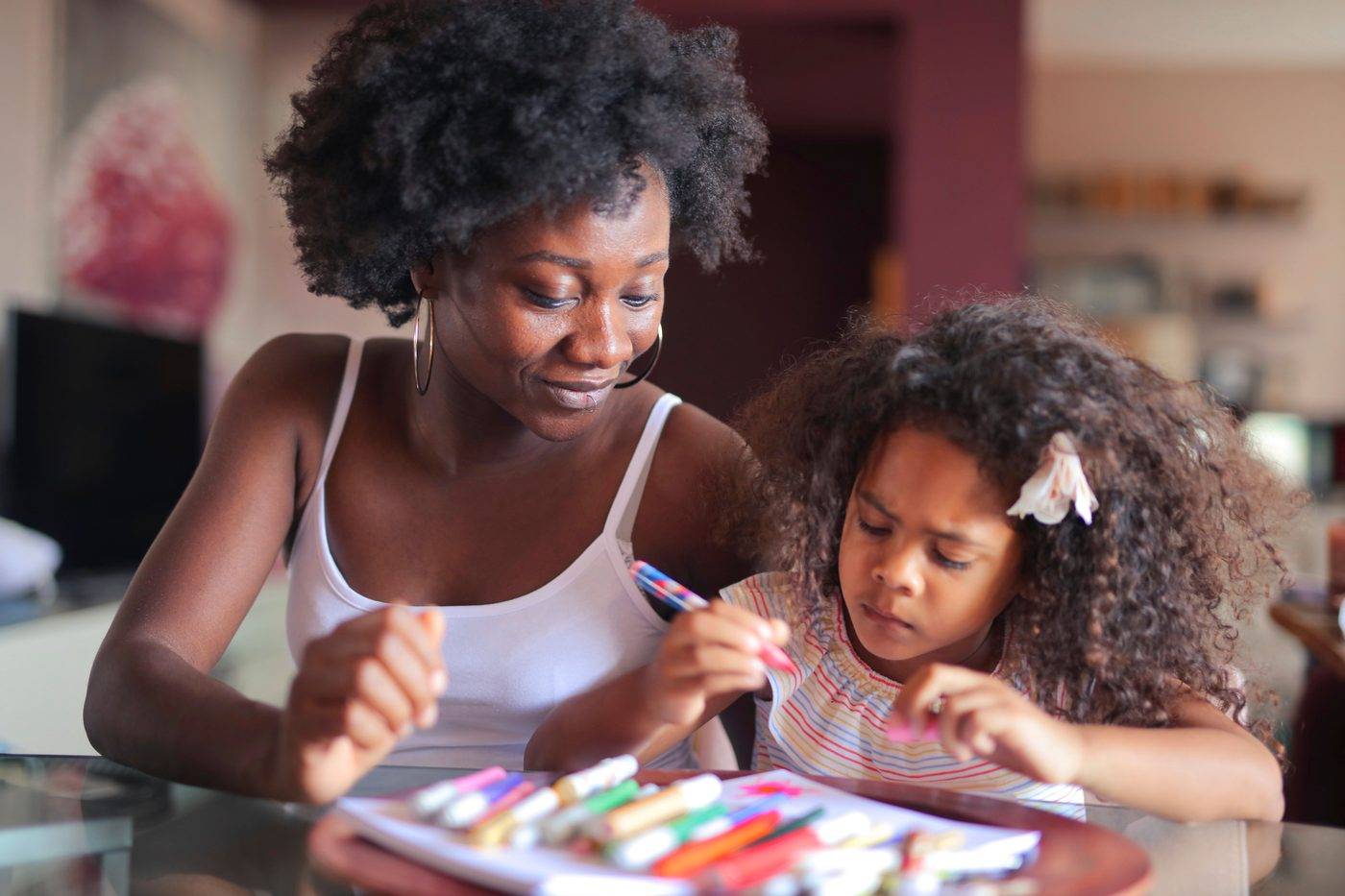 A mother and her young daughter drawing with markers at a table at home